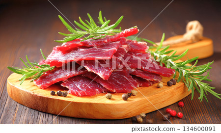 Thinly sliced raw beef, likely flank steak, appears on a wooden board amongst rosemary sprigs and various peppercorns 134600091