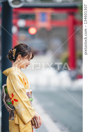 A young woman in traditional Japanese clothing with a torii gate in the background 134601307