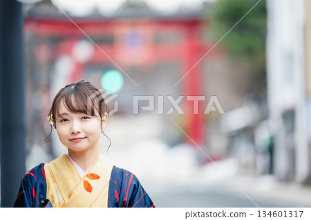 一位身著傳統日式服裝的年輕女子,背景是一座鳥居。 一位身著傳統日式服裝的年輕女子,背景是一座鳥居。 134601317