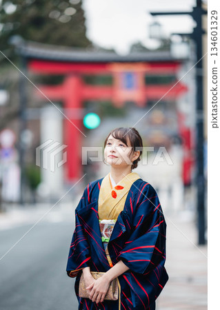 A young woman in traditional Japanese clothing with a torii gate in the background 134601329