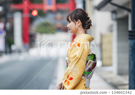 A young woman in traditional Japanese clothing with a torii gate in the background 134601342