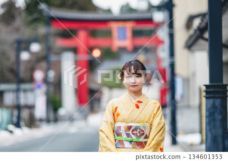 A young woman in traditional Japanese clothing with a torii gate in the background 134601353