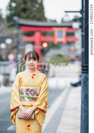 A young woman in traditional Japanese clothing with a torii gate in the background 134601354
