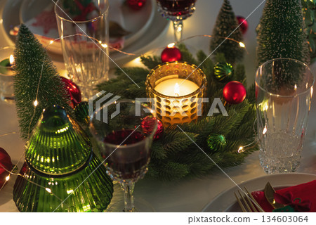 Festive Holiday Table Setting with Candle Lights and Decorations against Christmas Tree Festive Holiday Table Setting with Candle Lights and Decorations against Christmas Tree 134603064