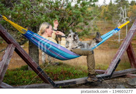 Woman relaxing in hammock with dog wearing outdoor clothing in forest nature 134603277