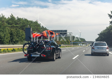 Back view modern black family wagon van car with mounted roof kayak and bike tail carrier driving european highway road against blue sky summer day. Lifestyle travel adventure trip journey concept Back view modern black family wagon van car with mounted roof kayak and bike tail carrier driving european highway road against blue sky summer day. Lifestyle travel adventure trip journey concept 134604605