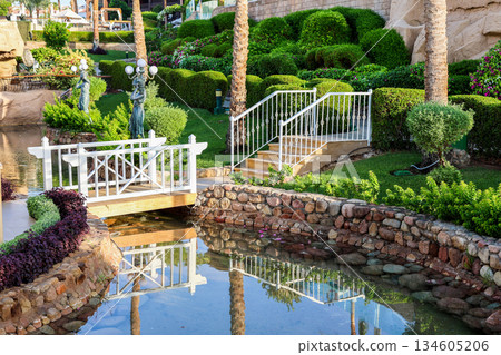 A green area with a garden and a bridge over a pond A green area with a garden and a bridge over a pond 134605206