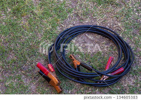 Jumper cables coiled on the ground. Concept of elements for travel safety. Jumper cables coiled on the ground. Concept of elements for travel safety. 134605383