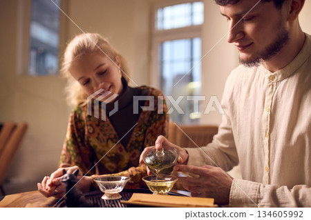 Man pouring tea into ceramic cup during calm home ritual. 134605992