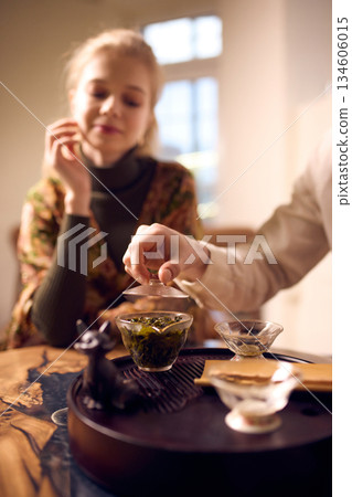 Man opening glass teapot while woman watches tea brewing process indoors 134606015