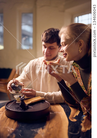 Young couple performing traditional tea ritual with glass teaware at wooden table. Young couple performing traditional tea ritual with glass teaware at wooden table. 134606043