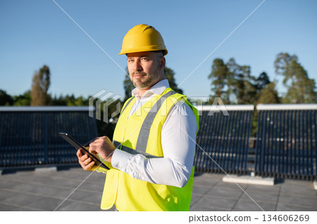 Worker inspecting rooftop solar panels holding digital tablet in hands Worker inspecting rooftop solar panels holding digital tablet in hands 134606269