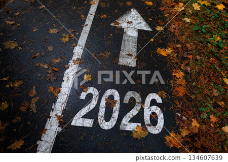 Road marking with the number 2026 and an arrow pointing forward, symbolizing future, progress, and new beginnings. Autumn leaves scattered on the path. New Year 2026, creative idea. Road marking with the number 2026 and an arrow pointing forward, symbolizing future, progress, and new beginnings. Autumn leaves scattered on the path. New Year 2026, creative idea. 134607639