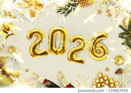New Year 2026, creative idea. Golden balloons 2026 lie on a beige concrete table with fireplaces, candies, a golden disco ball, champagne and a Christmas tree, top view. Christmas card 2026 134607656