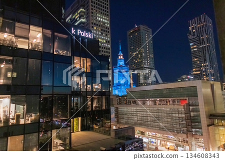 Stunning night view of Warsaw's contrasting architecture. Modern office towers surround the historic Palace of Culture and Science. A bright Bank Polski sign is visible. Polish capital, urban, finance Stunning night view of Warsaw's contrasting architecture. Modern office towers surround the historic Palace of Culture and Science. A bright Bank Polski sign is visible. Polish capital, urban, finance 134608343