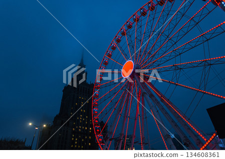 Illuminated Ferris wheel in Warsaw at twilight, featuring the Palace of Culture and Science in a misty blue hour. Captivating urban cityscape for travel blogs, tourism ads, and European city guides Illuminated Ferris wheel in Warsaw at twilight, featuring the Palace of Culture and Science in a misty blue hour. Captivating urban cityscape for travel blogs, tourism ads, and European city guides 134608361