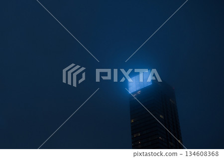 Minimalist urban architecture featuring blue light geometry on a dark background. clean, low-angle perspective of a dark building's facade reaching into a hazy sky. The blue light at foggy evening 134608368