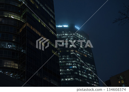 Night view of modern urban skyscrapers with glowing office windows. Tall glass buildings rise against a deep blue sky, cityscape. business, technology, architecture, and metropolitan life. Night view of modern urban skyscrapers with glowing office windows. Tall glass buildings rise against a deep blue sky, cityscape. business, technology, architecture, and metropolitan life. 134608374
