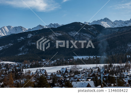 Picturesque Zakopane, a Polish mountain resort. Snowy homes and dark forests contrast with the sharp, white peaks of the Tatra Mountains (Tatry) 134608422