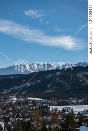 Traditional wooden houses and snowy roofs of Zakopane, Poland, snow-capped peaks of the Tatra Mountains. European winter resort town. Sunny winter holidays 134608423