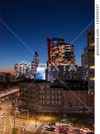 Warsaw cityscape at blue hour twilight. Modern skyscrapers overlook an old building and a busy street intersection with moving traffic. Dramatic urban contrast, Poland architecture, evening time 134608447
