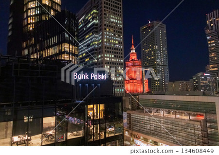 Modern Warsaw skyline at night, highlighting the illuminated Bank Polski sign amidst sleek glass high-rises. The iconic Palace of Culture and Science (PKiN) stands in the background. Finance, architec Modern Warsaw skyline at night, highlighting the illuminated Bank Polski sign amidst sleek glass high-rises. The iconic Palace of Culture and Science (PKiN) stands in the background. Finance, architec 134608449
