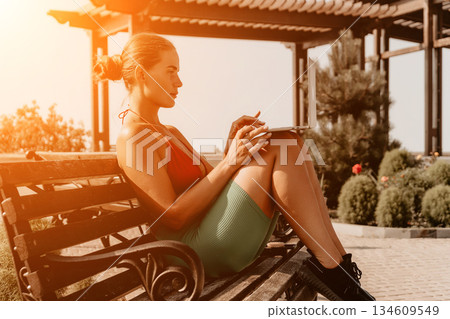 Woman, Park, Notebook - A woman in sportswear sits on a bench in a park writing in a notebook on a sunny day. Woman, Park, Notebook - A woman in sportswear sits on a bench in a park writing in a notebook on a sunny day. 134609549