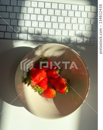 Fresh strawberries in bowl with sunlight on workspace table. Natural light mood, healthy snack choice and balanced workday lifestyle with minimal food composition. Fresh strawberries in bowl with sunlight on workspace table. Natural light mood, healthy snack choice and balanced workday lifestyle with minimal food composition. 134612438