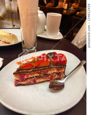 Strawberry layered cake served on plate in cafe interior. Dessert indulgence, sweet break, cozy dining moment and relaxed lifestyle enjoyment with pastry details. Strawberry layered cake served on plate in cafe interior. Dessert indulgence, sweet break, cozy dining moment and relaxed lifestyle enjoyment with pastry details. 134612459