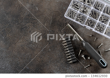 Manual screwdriver, drill bits and assorted screws on dark textured table. DIY home tools. Top view. Copy space. 134612930