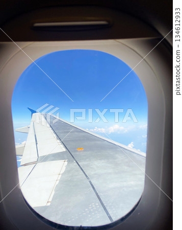 Airplane wing seen through window above clouds and sky. Travel journey, aviation perspective, freedom, movement, and modern transportation experience 134612933