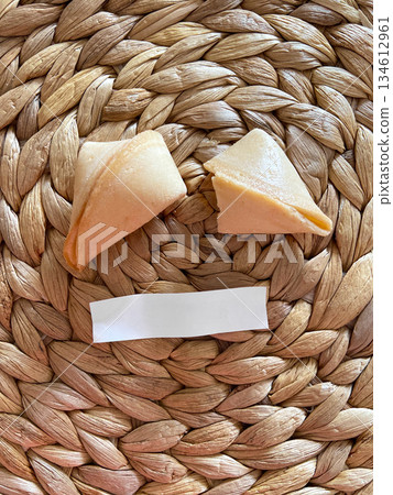 Fortune cookies placed on woven straw surface with blank message strip. Symbolic food styling, anticipation, curiosity and minimalist still life composition 134612961