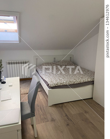 Minimal attic bedroom with bed and workspace in apartment. Simple interior design, functional living space and calm home lifestyle emphasizing order and comfort. Minimal attic bedroom with bed and workspace in apartment. Simple interior design, functional living space and calm home lifestyle emphasizing order and comfort. 134612976