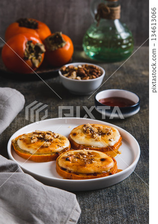 Delicious baked persimmon with cottage cheese, nuts and honey on a plate vertical view Delicious baked persimmon with cottage cheese, nuts and honey on a plate vertical view 134613066