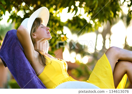 Young woman relaxing outdoors on sunny summer day. Happy lady lying down on comfortable beach chair daydreaming thinking. Calm beautiful smiling girl enjoying fresh air relaxing with closed eyes. 134613076