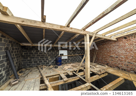 Two-storied building under construction and renovation. Perspective view of energy saving walls of large hollow foam insulation blocks and bricks, temporary wooden scaffolding, beams as roof frame. 134613165