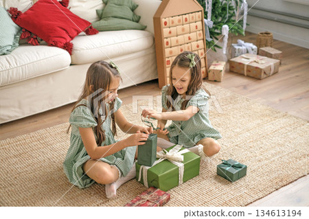 Little sister girls unwrap holiday gift boxes from Santa Claus early Christmas morning Little sister girls unwrap holiday gift boxes from Santa Claus early Christmas morning 134613194