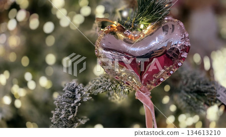 Festive heart ornament on christmas tree with twinkling lights. Horizontal banner. Copy space. Free space for text Festive heart ornament on christmas tree with twinkling lights. Horizontal banner. Copy space. Free space for text 134613210