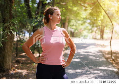 Woman Exercising Outdoors with Earbuds in Sunny Park 134613399