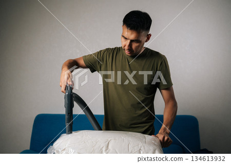 Portrait of man using vacuum cleaner to extract air from storage bag filled with bedding, positioned on ironing board, creating efficient space-saving storage solution. Concept of household chores 134613932
