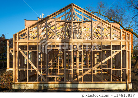 Wooden frame house under construction in urban area with blue sky and apartment buildings Wooden frame house under construction in urban area with blue sky and apartment buildings 134613937