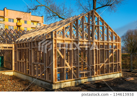 Wooden house frame under construction with roof trusses on urban building site Wooden house frame under construction with roof trusses on urban building site 134613938