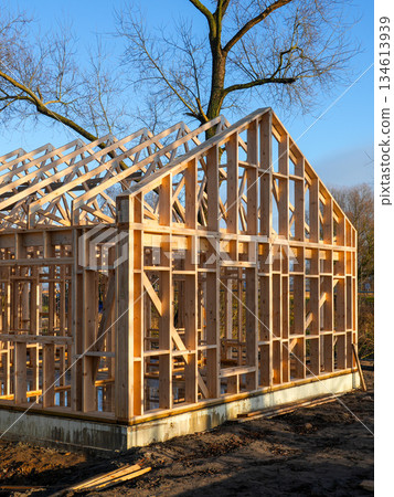 Wooden residential house frame under construction on urban site with blue sky and sunlight Wooden residential house frame under construction on urban site with blue sky and sunlight 134613939
