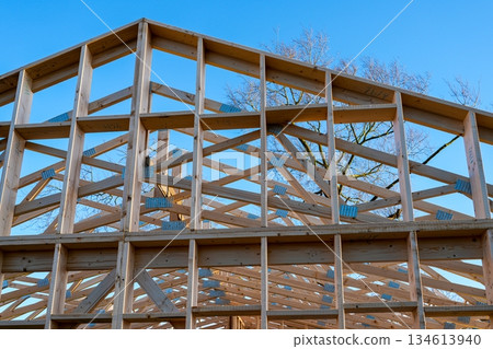Wooden house roof truss and timber frame under construction against clear blue sky Wooden house roof truss and timber frame under construction against clear blue sky 134613940