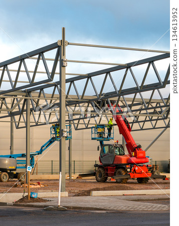 Workers assembling steel frame with crane and lifts during construction of industrial building 134613952