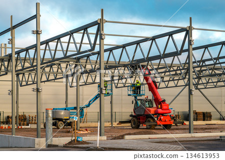 Industrial warehouse steel frame construction with crane and aerial lifts on active building site 134613953