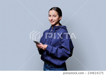 Portrait of smiling teenage girl holding smartphone on gray studio background 134614173