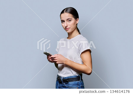 Portrait of smiling teenage girl using smartphone on gray studio background 134614176