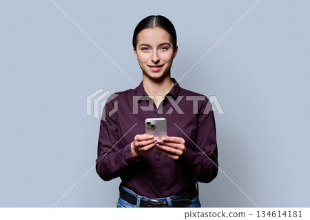 Portrait of smiling teenage girl holding smartphone on gray studio background 134614181