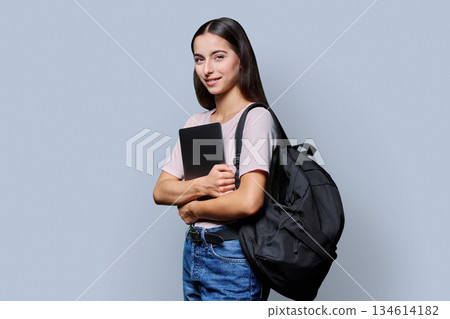Portrait of beautiful female teenage student with backpack, laptop on gray background Portrait of beautiful female teenage student with backpack, laptop on gray background 134614182